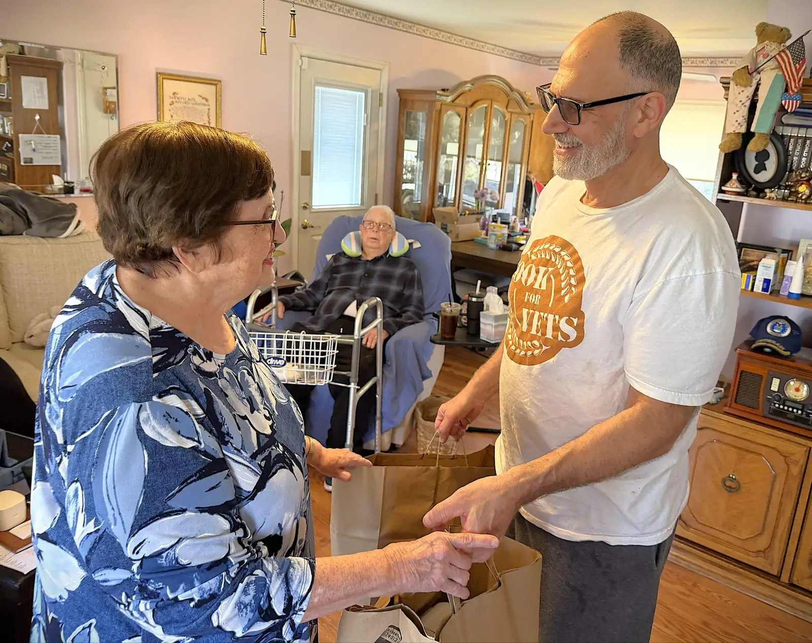 A Cook For Vets volunteer hands paper grocery bags to a resident at home.