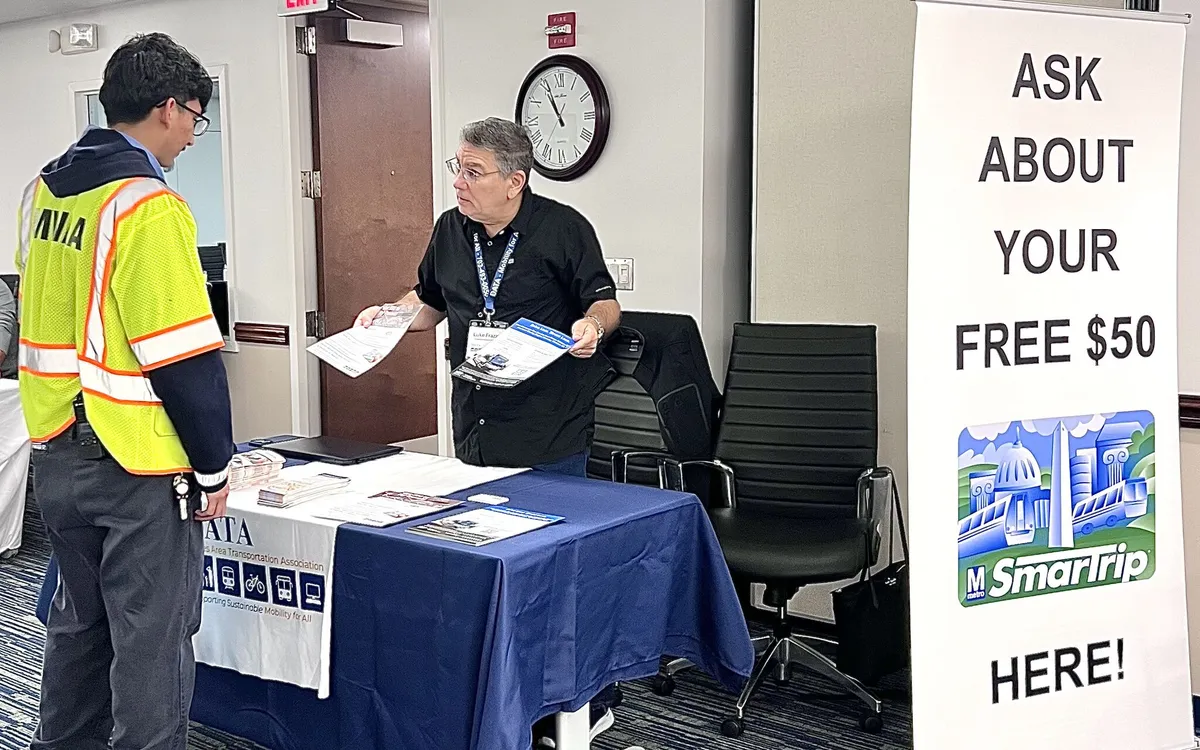 A DATA staff member at an outreach table beside a Free $50 SmarTrip banner.