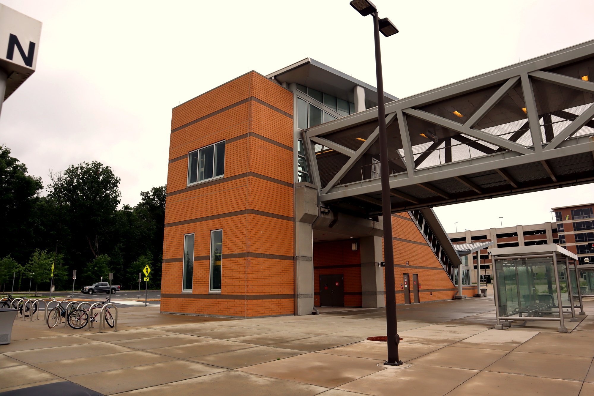 A Metro station entrance with a pedestrian bridge to a parking garage, bike racks holding several bicycles, and a glass bus shelter.