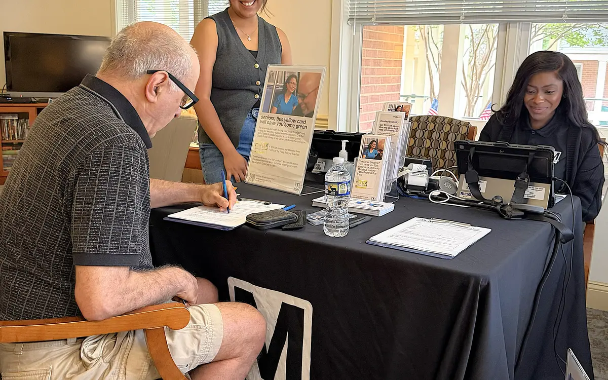 An older man fills out a form at a mobility services outreach table while two staff members help.