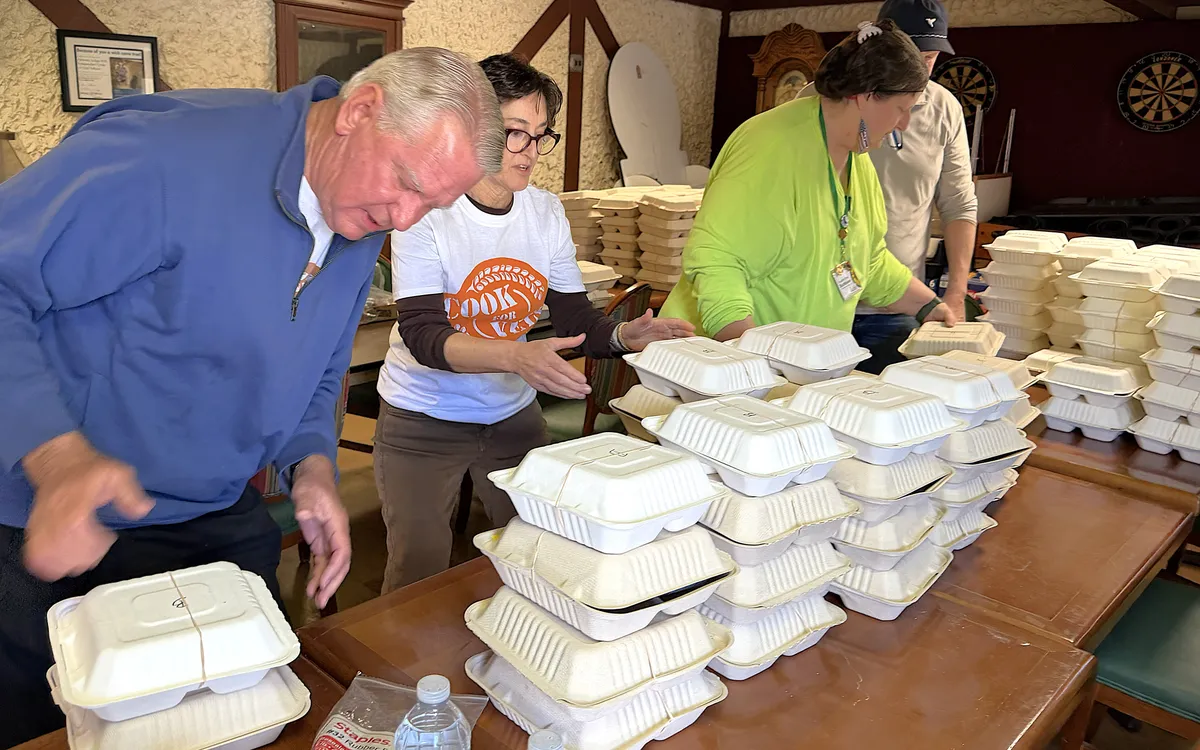 Volunteers assembling stacks of packaged meals on a table.