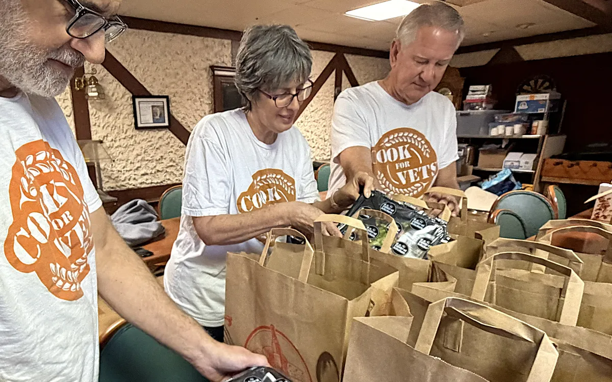 Three volunteers in Cook For Vets shirts packing grocery bags with food.