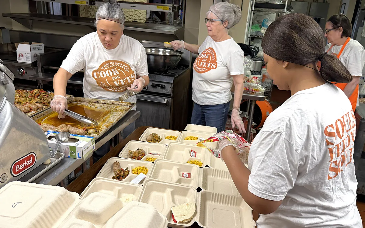 Volunteers plating meals into takeout containers in a kitchen.