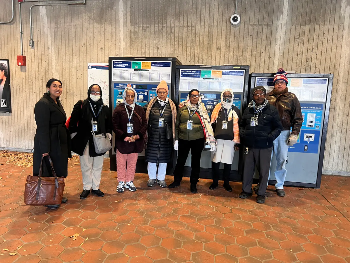 A group of older adults wearing lanyards standing beside Metro fare machines during a guided transit outing.