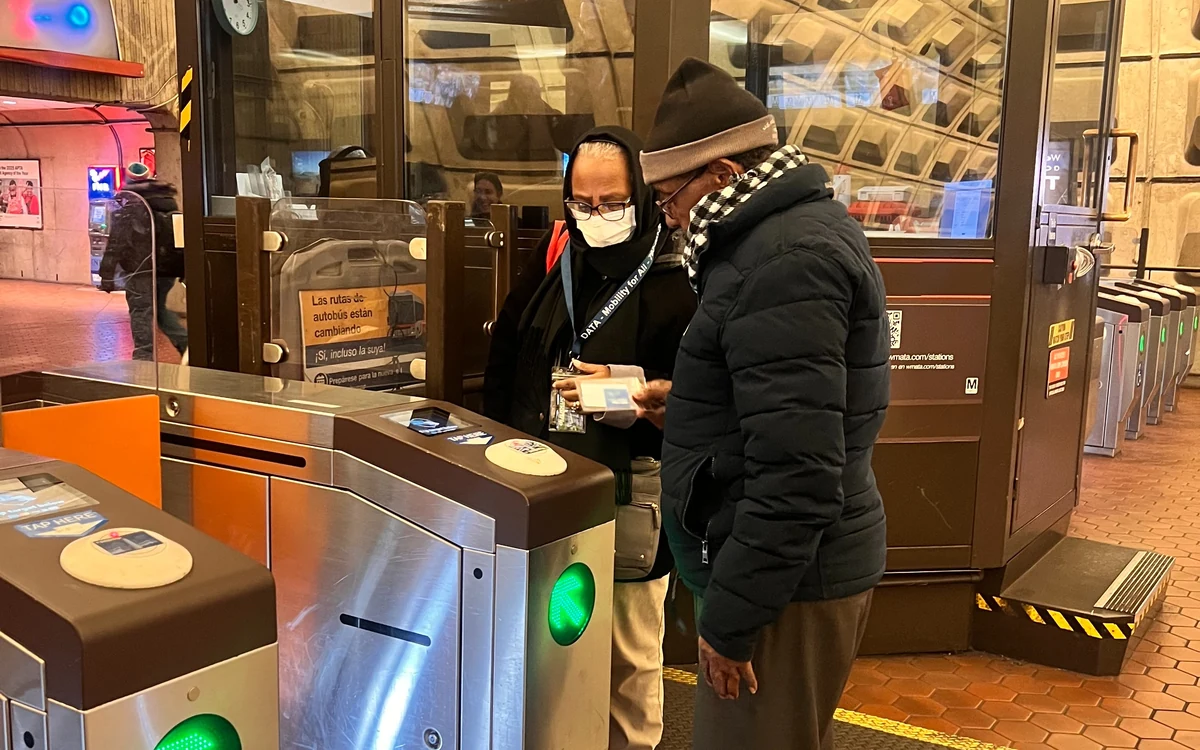 A DATA staff member helping an older rider tap through a Metro faregate.