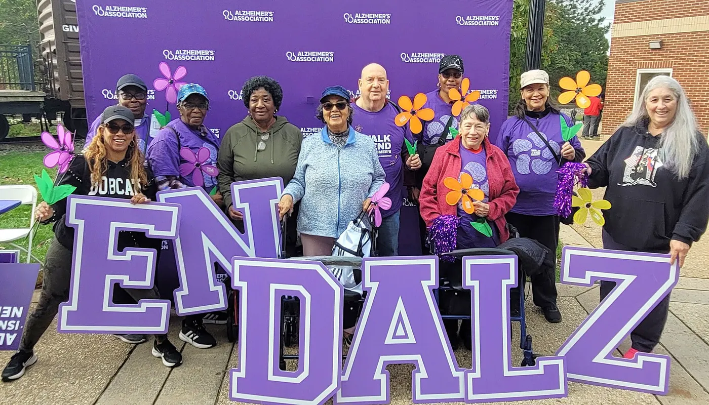 Older adults holding large END ALZ letters and paper flowers at an Alzheimer's Association walk.